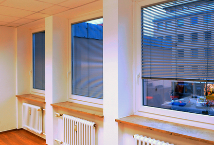 Innenansicht einer Fensterfront in einer Praxis mit drei heruntergelassenen Innenjalousien in grau