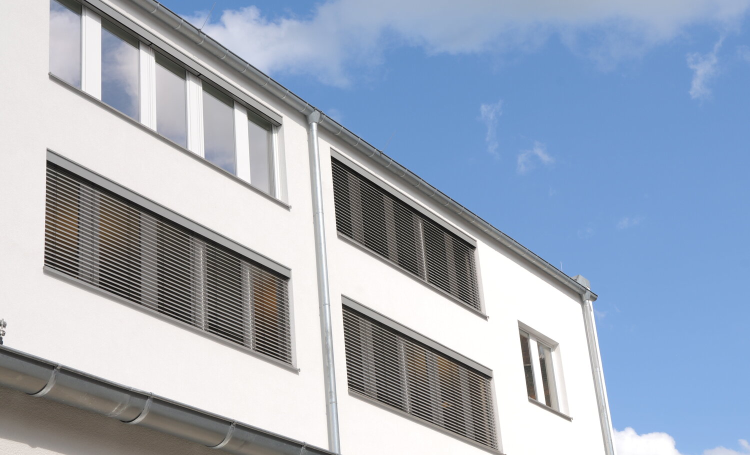 Ansicht eines Bürohauses mit Außenjalousien, teils ganz heruntergelassen – an einem Fenster hochgefahren Ansicht eines Bürohauses mit Außenjalousien, teils ganz heruntergelassen – an einem Fenster hochgefahren