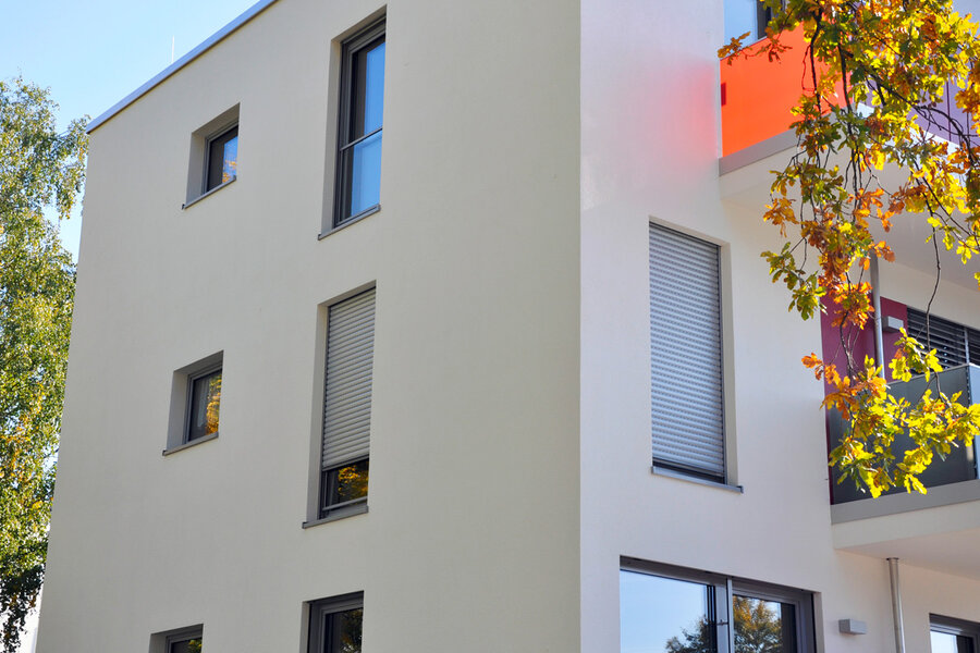 Fassade eines öffentlichen Gebäudes mit Außenrollläden vor den Fenstern, teilweise herunter gelassen.