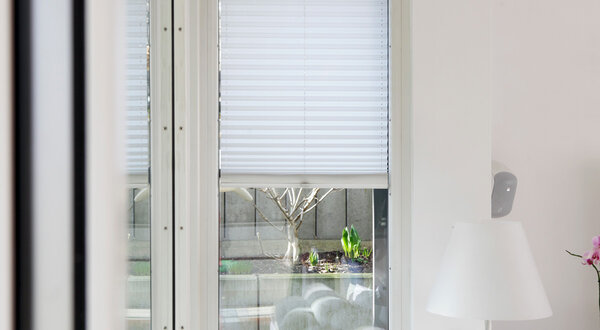 Weißes Plisee vor Fenster eines Wohnhauses halbhochgezogen