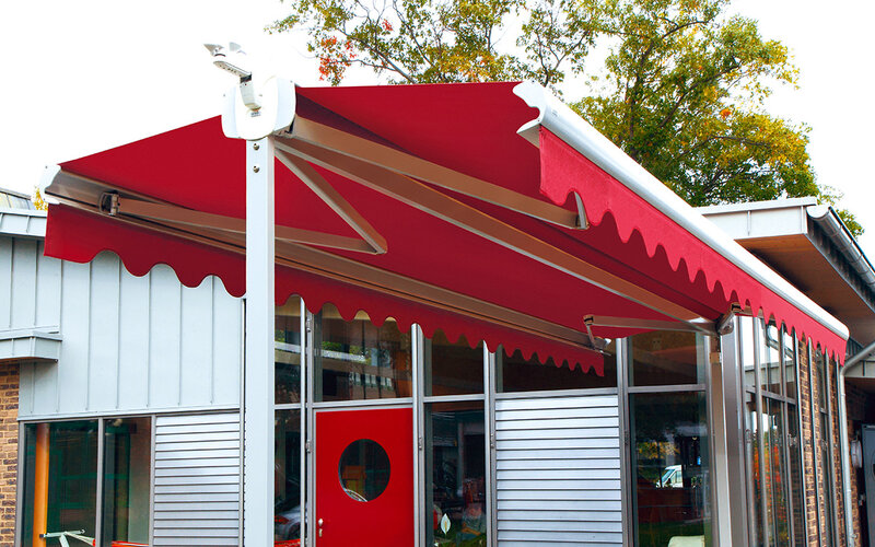 Detailansicht einer ausgefahrenen Doppelmarkise mit dunkelblauem Stoff und weißer Metallkonstruktion Detailansicht einer ausgefahrenen Doppelmarkise mit dunkelblauem Stoff und weißer Metallkonstruktion