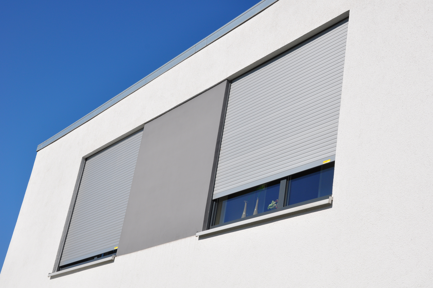 Außenansicht zweier Fenster eines Bürohauses mit heruntergelassenen Rollläden in lichtgrau Außenansicht zweier Fenster eines Bürohauses mit heruntergelassenen Rollläden in lichtgrau