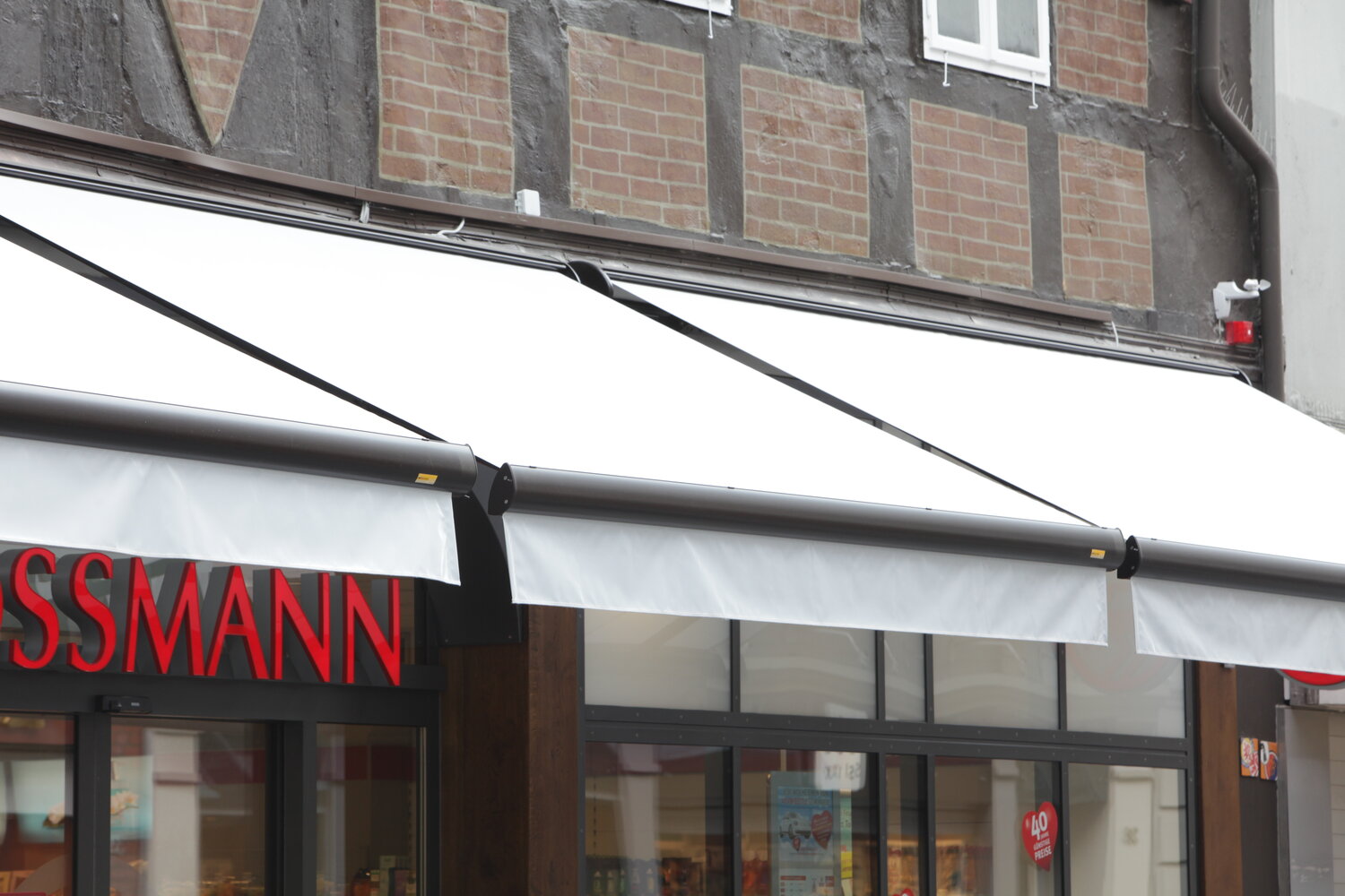 Ausgefahrene Ladenmarkisen in weiß, vor der Fassade eines Einzelhandelsgeschäftes zum Schutz vor Sonne und der Produkte Ausgefahrene Ladenmarkisen in weiß, vor der Fassade eines Einzelhandelsgeschäftes zum Schutz vor Sonne und der Produkte