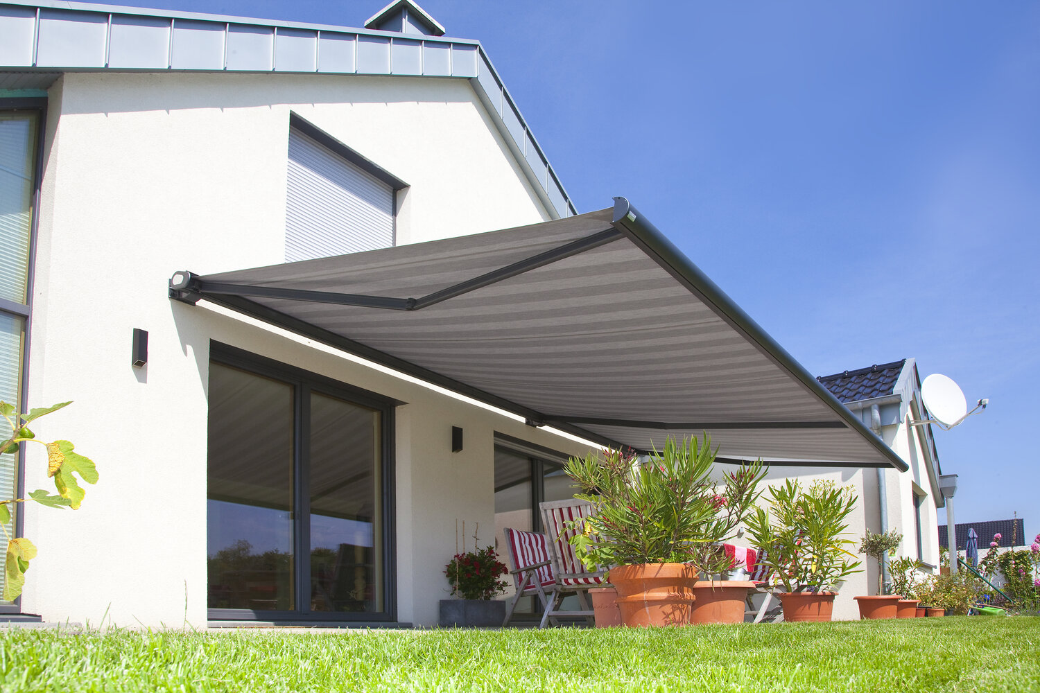 Terrassenansicht eines Einfamilienhauses mit einer ausgefahrenen Gelenkarmmarkise in grau Terrassenansicht eines Einfamilienhauses mit einer ausgefahrenen Gelenkarmmarkise in grau
