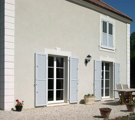 Schutz und Akzent: Haus mit bodentiefen Fenstern mit klassischen weißen Klappläden, beim Fenster im 1. O.G. geschlossen. Schutz und Akzent: Haus mit bodentiefen Fenstern mit klassischen weißen Klappläden, beim Fenster im 1. O.G. geschlossen.