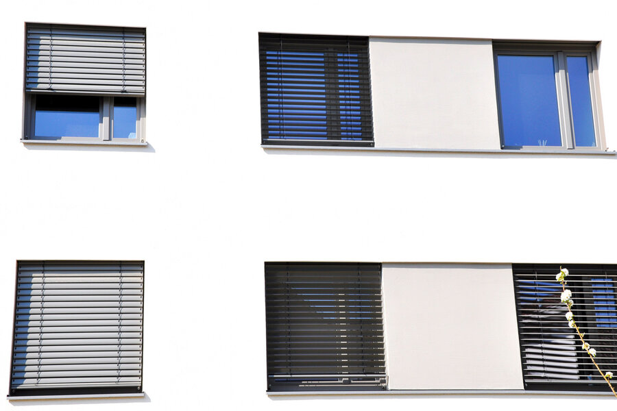 Fassade eines öffentlichen Gebäudes mit Außenjalousien jeweils eine Jalousie über vier bzw. fünf nebeneinander liegende Fenstern, teilweise herunter gelassen.