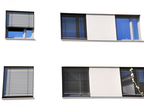 Fassade eines öffentlichen Gebäudes mit Außenjalousien jeweils eine Jalousie über vier bzw. fünf nebeneinander liegende Fenstern, teilweise herunter gelassen.