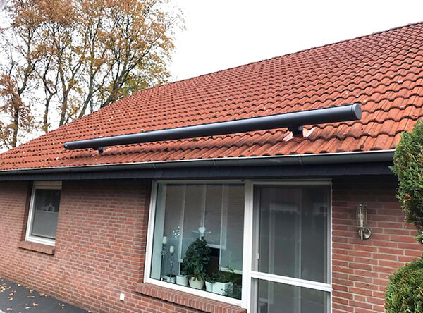 Auf dem unteren Rand des Daches eines einstöckigen Wohnhauses mit einer Sonderanfertigung montierte Markise, orange – weiß – rot gestreift.