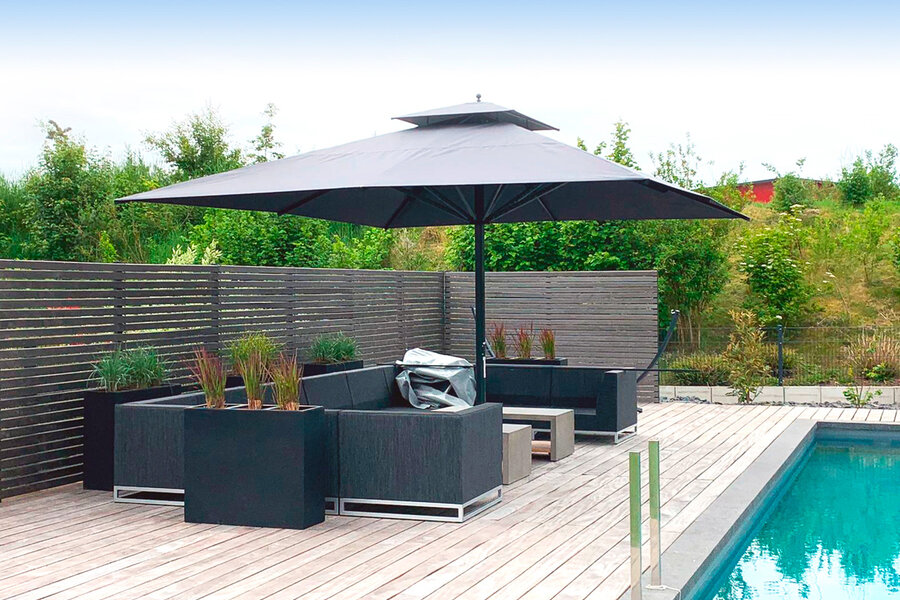 Aufgespannter Sonnenschirm Caravita mit Bodenhülse in schwarz auf der Terrasse neben Loungemöbelsitzgruppe