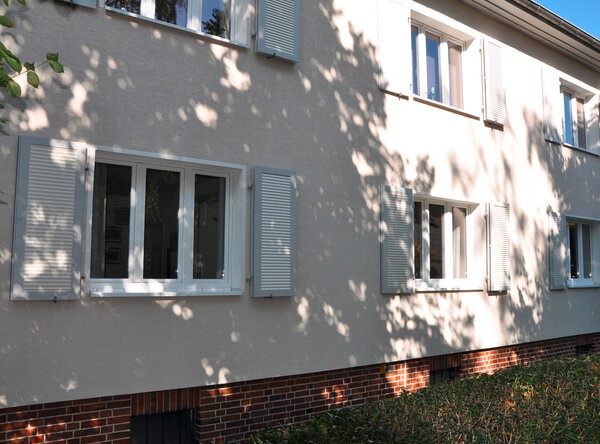 Klappläden in lichtgrau, offen und geschlossen vor den Fenstern eines Wohnhauses