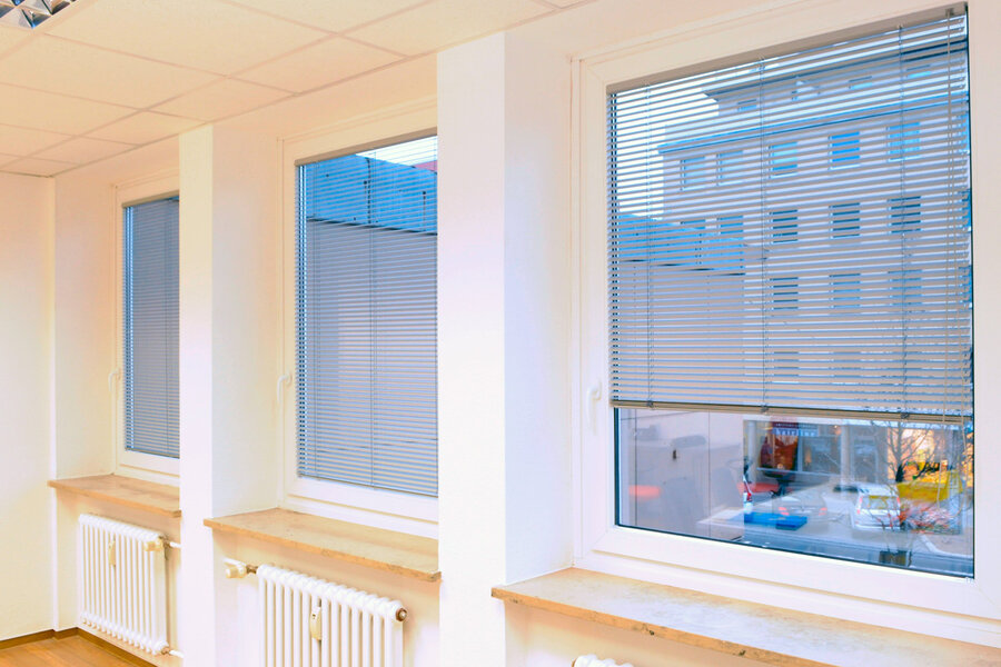 Ausblick durch drei Fenster eines Raumes mit heruntergelassenen Innenjalousien in weiß