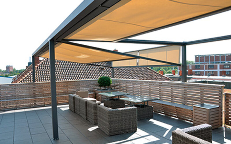 Das freistehende Beschattungssystem Q,Bus auf einer Dachterrasse mit schwarzer Metallkonstruktion und Markisen in beige. Das freistehende Beschattungssystem Q,Bus auf einer Dachterrasse mit schwarzer Metallkonstruktion und Markisen in beige.