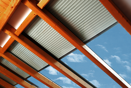 Zur Hälfte herabgelassene Dachfenster-Rollläden an einer Glasdachfront mit Holzbalken Unterkonstruktion